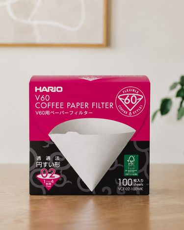 Box of Hario V60 coffee paper filters on a wooden surface with a white wall background.