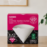 Box of Hario V60 coffee paper filters on a wooden surface with a white wall background.